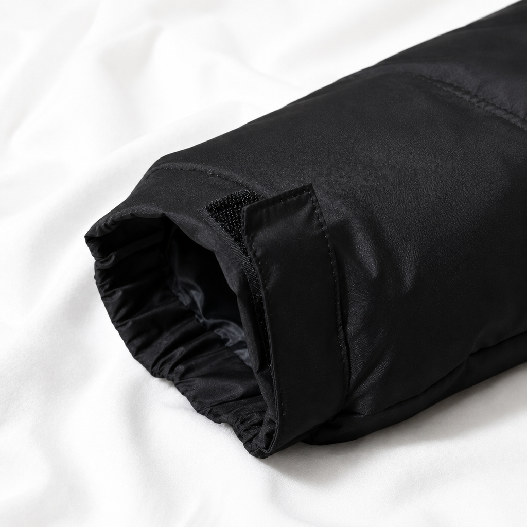 Close-up of a black puffer jacket sleeve with an adjustable Velcro cuff displayed on a soft white cloth background, highlighting the insulated design and weather-resistant finish.