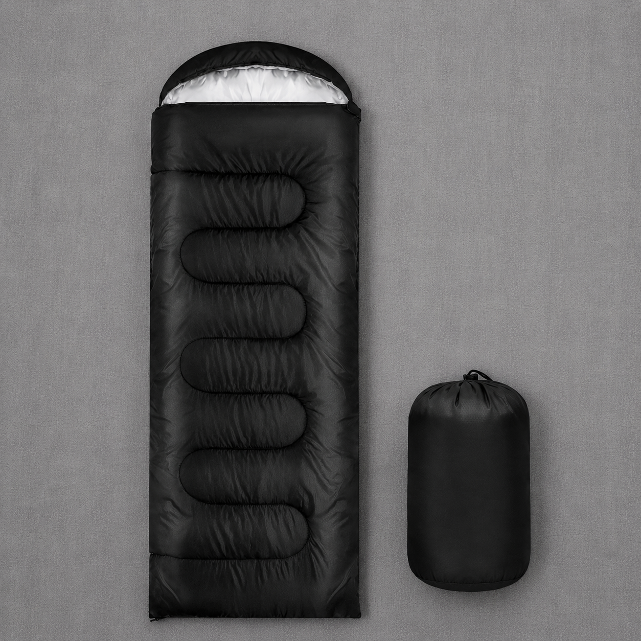 Black waterproof sleeping bag with matching carry bag displayed on a grey cloth background, showcasing the hooded design and compact storage sack.